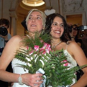 Two women smiling with flowers on their wedding day.