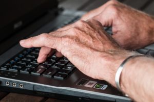 Older person's hands typing at a computer.