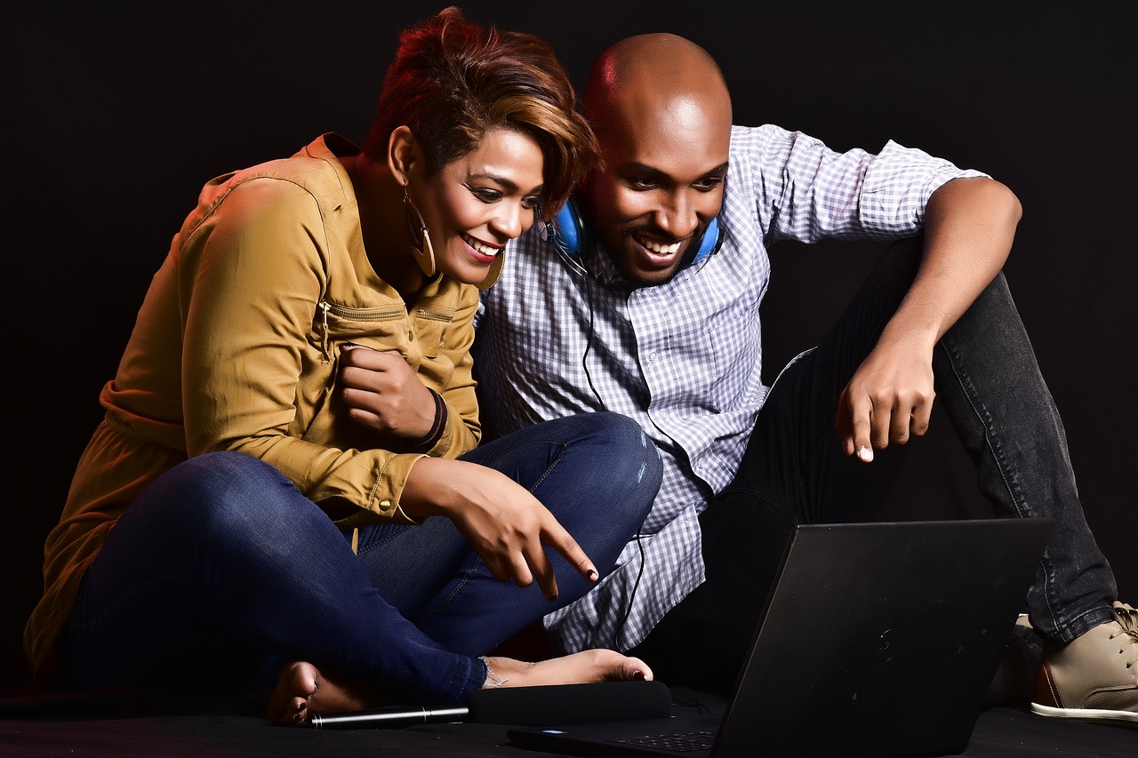 Man and woman looking happily at a computer with a microphone close-by, presumably working on music development.