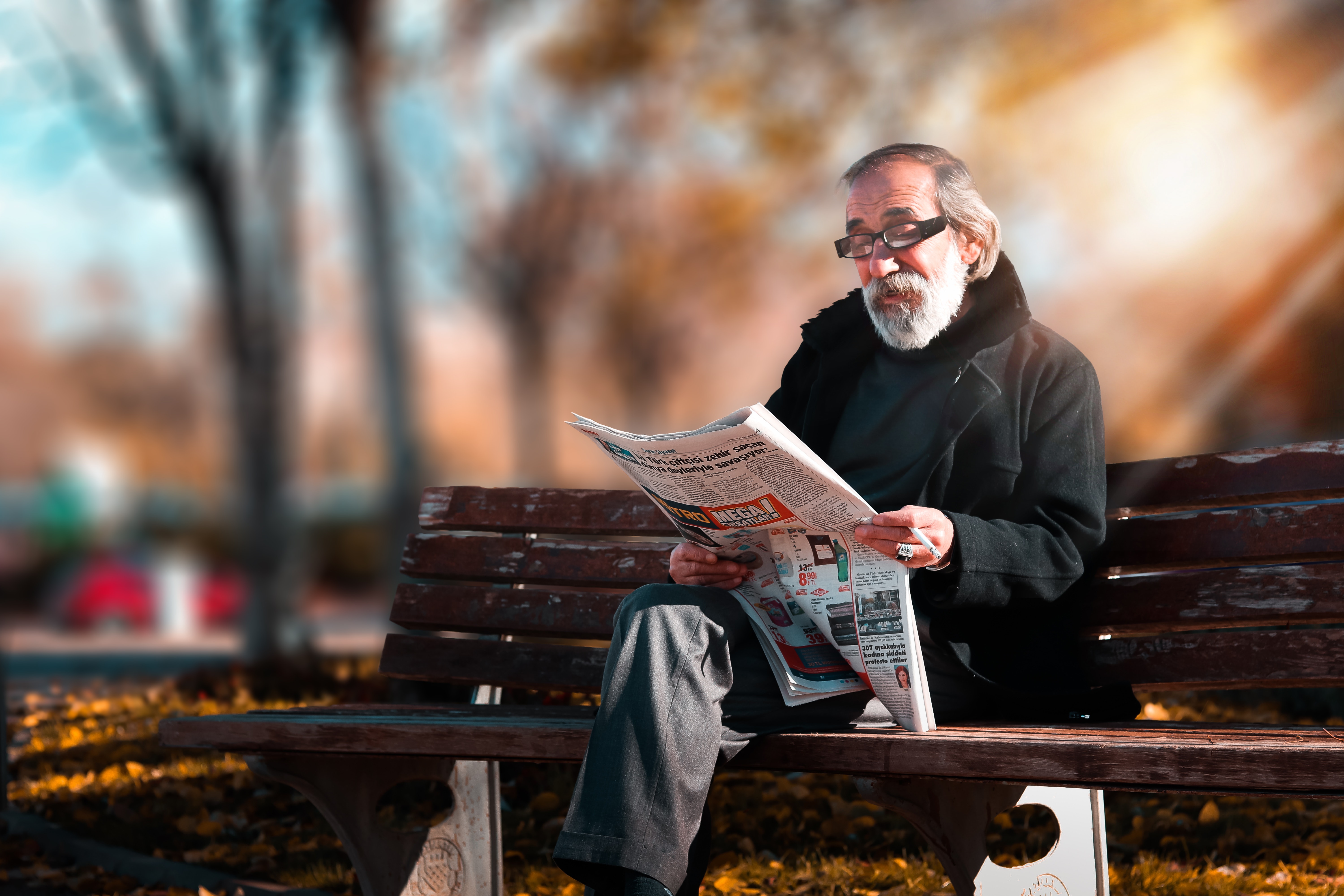 Elderly man reading the newspaper on a park bench.