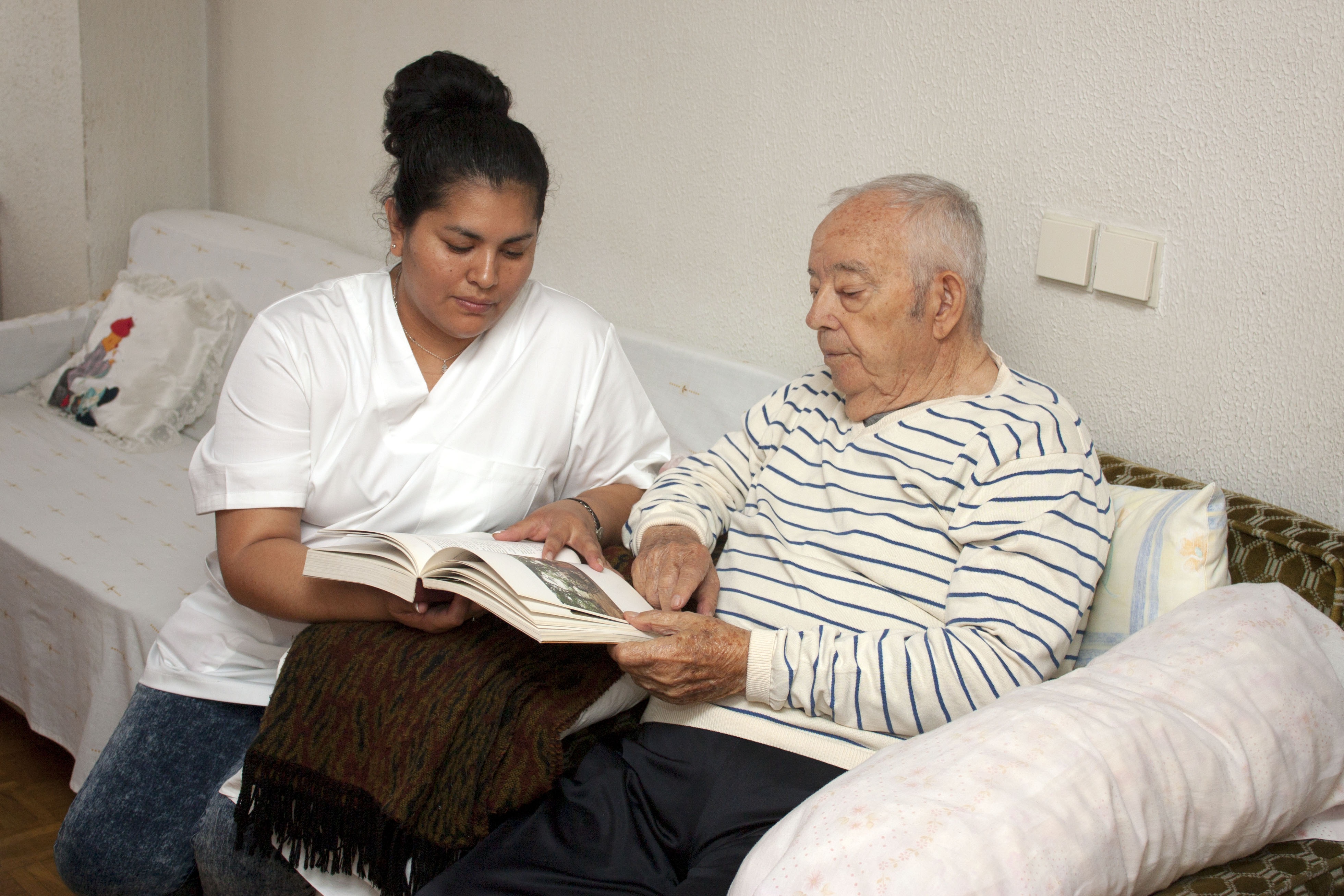 A woman is assisting an elderly man in reading a book