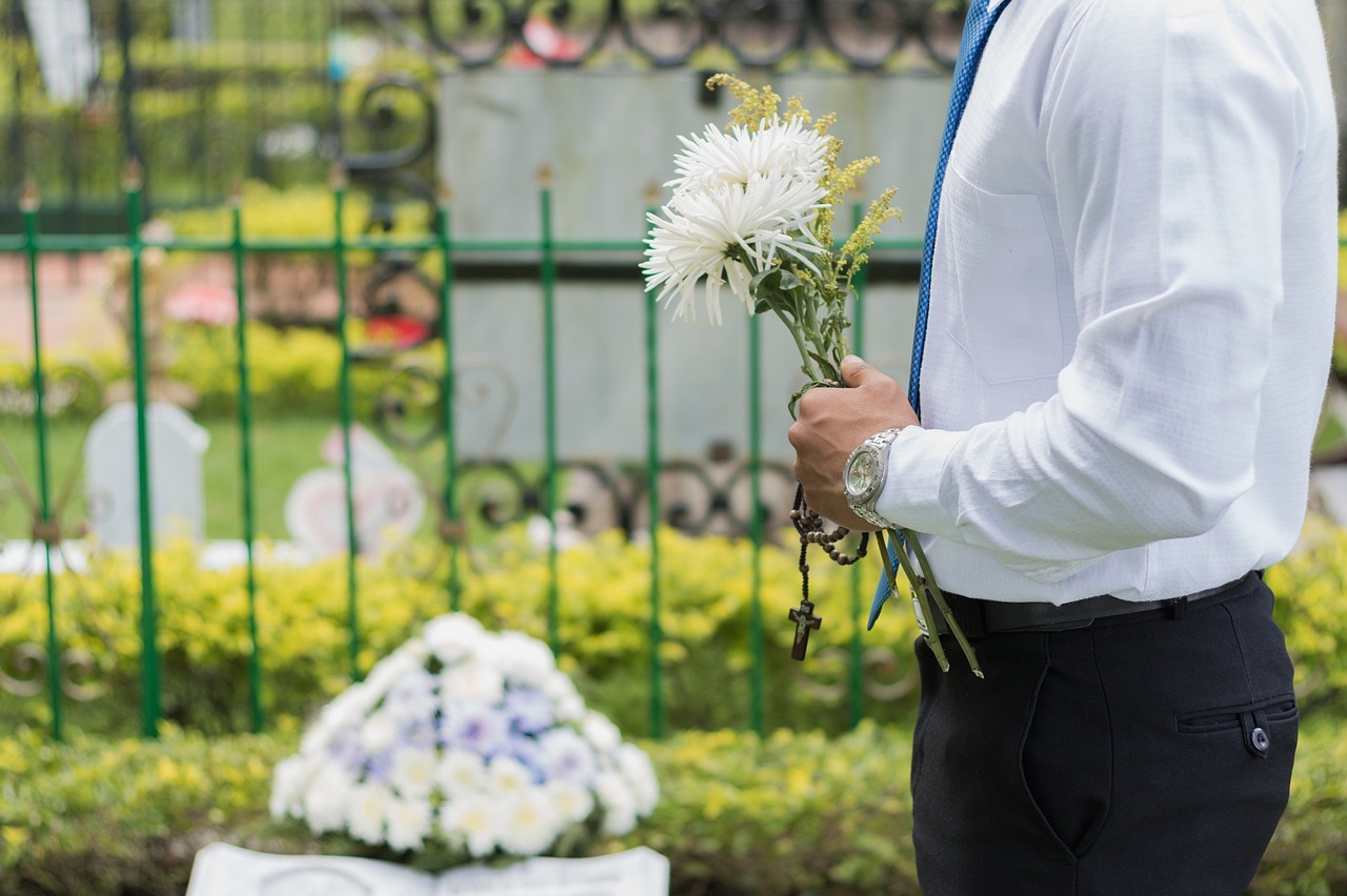 Man holds flowers at a grave.