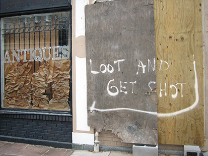 Uma foto de uma casa danificada pelo furacão Katrina com uma placa afixada na cerca que diz: “Saqueadores serão baleados