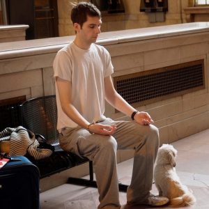 A young man meditates on a bench in a train station." title="A young man meditates on a bench in a train station.