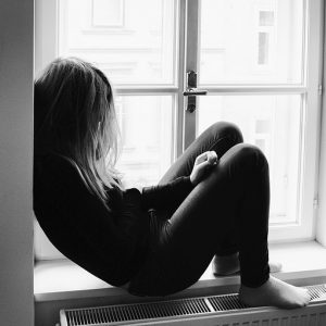 A young women sits alone on a windowsill.