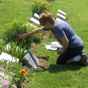 Una mujer se arrodilla frente a una lápida en un cementerio.