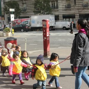 Un grupo de estudiantes de preescolar son guiados por una calle de la ciudad por un adulto.