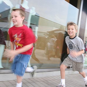 Two young boys sprint along a sidewalk.