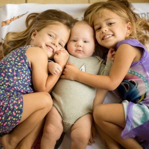 Las hermanas gemelas abrazan a su hermano pequeño.