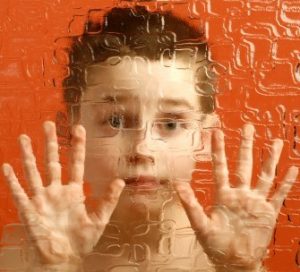 A boy looks out from behind textured glass.