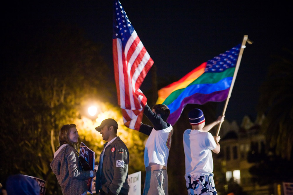 La figure (c) montre des personnes brandissant un drapeau américain et un drapeau arc-en-ciel.