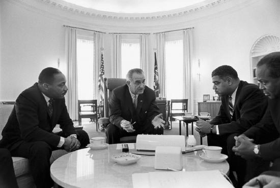 Lyndon B. Johnson sitting in the Oval Office with Martin Luther King Jr. and other Black leaders.