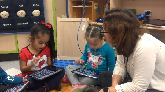 children with iPads sitting on floor with teacher