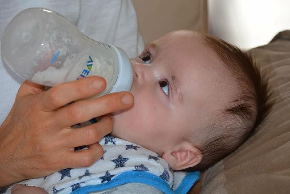 infant being bottle fed looking up towards adult