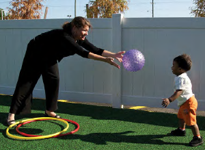 adult tossing ball toward a toddler outside