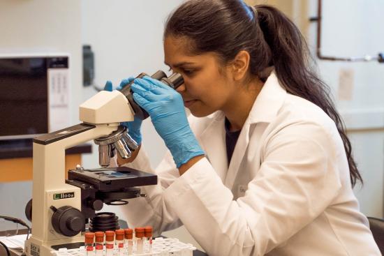 A woman in a labcoat examines something with a microscope.