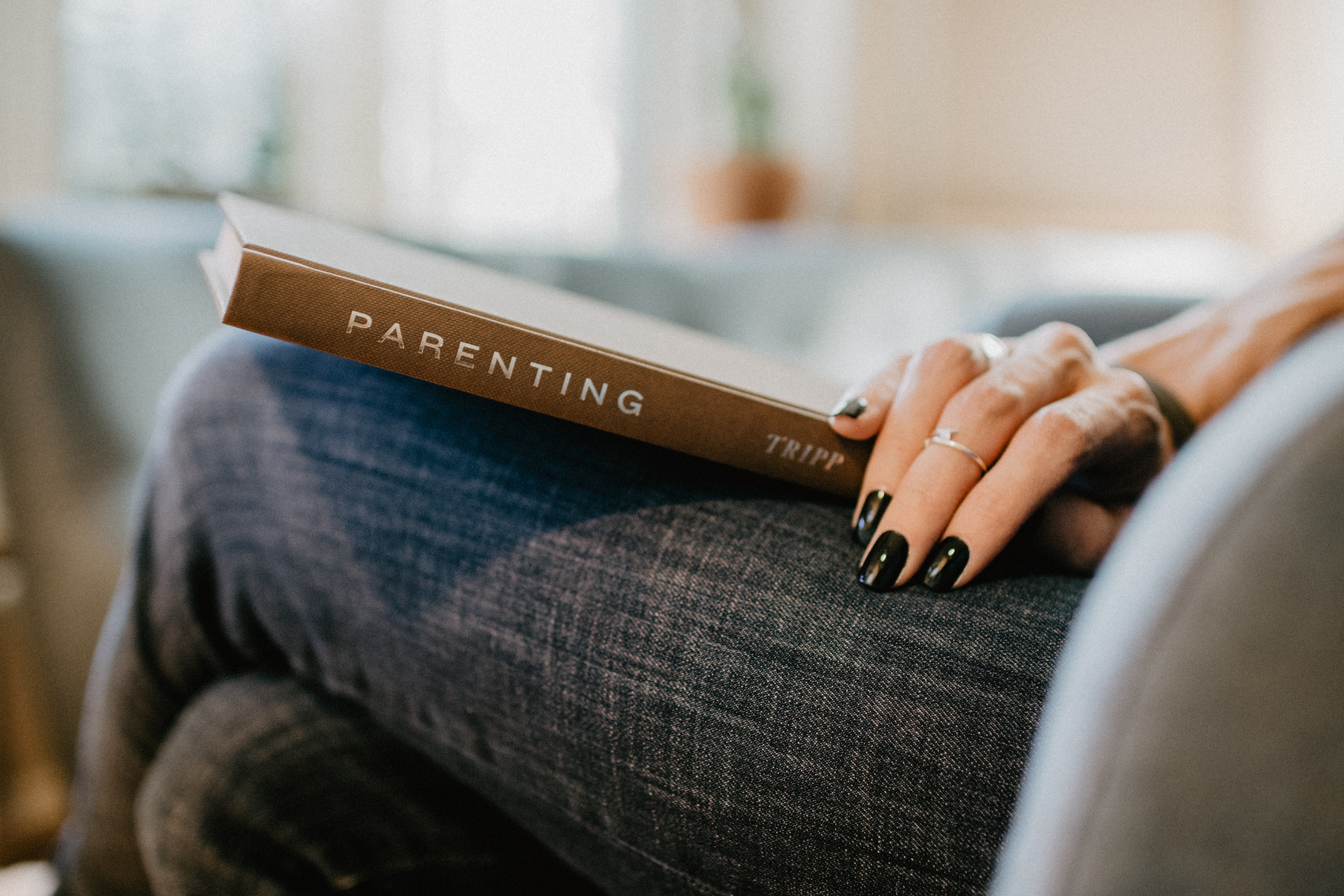  A book titled "parenting" sits on a woman's lap.