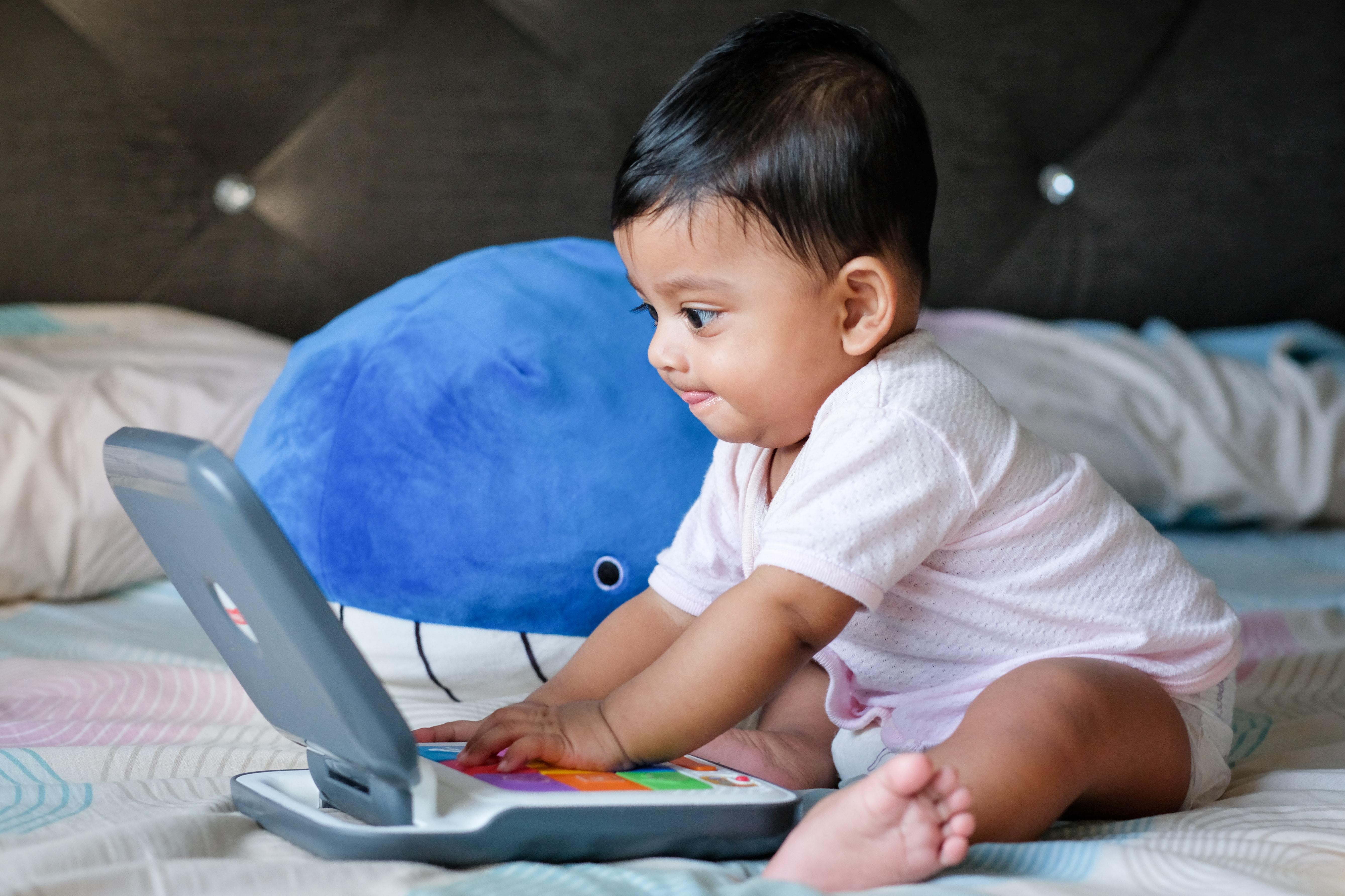 A smiling baby sits in front of a toy computer.