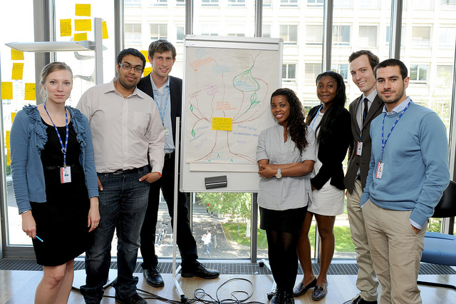 A group of seven professionally-dressed college students stand in front of a poster during a workshop.