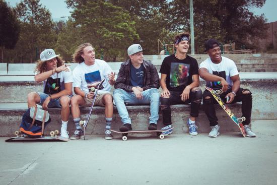 Five males with skateboards sit on a bench.