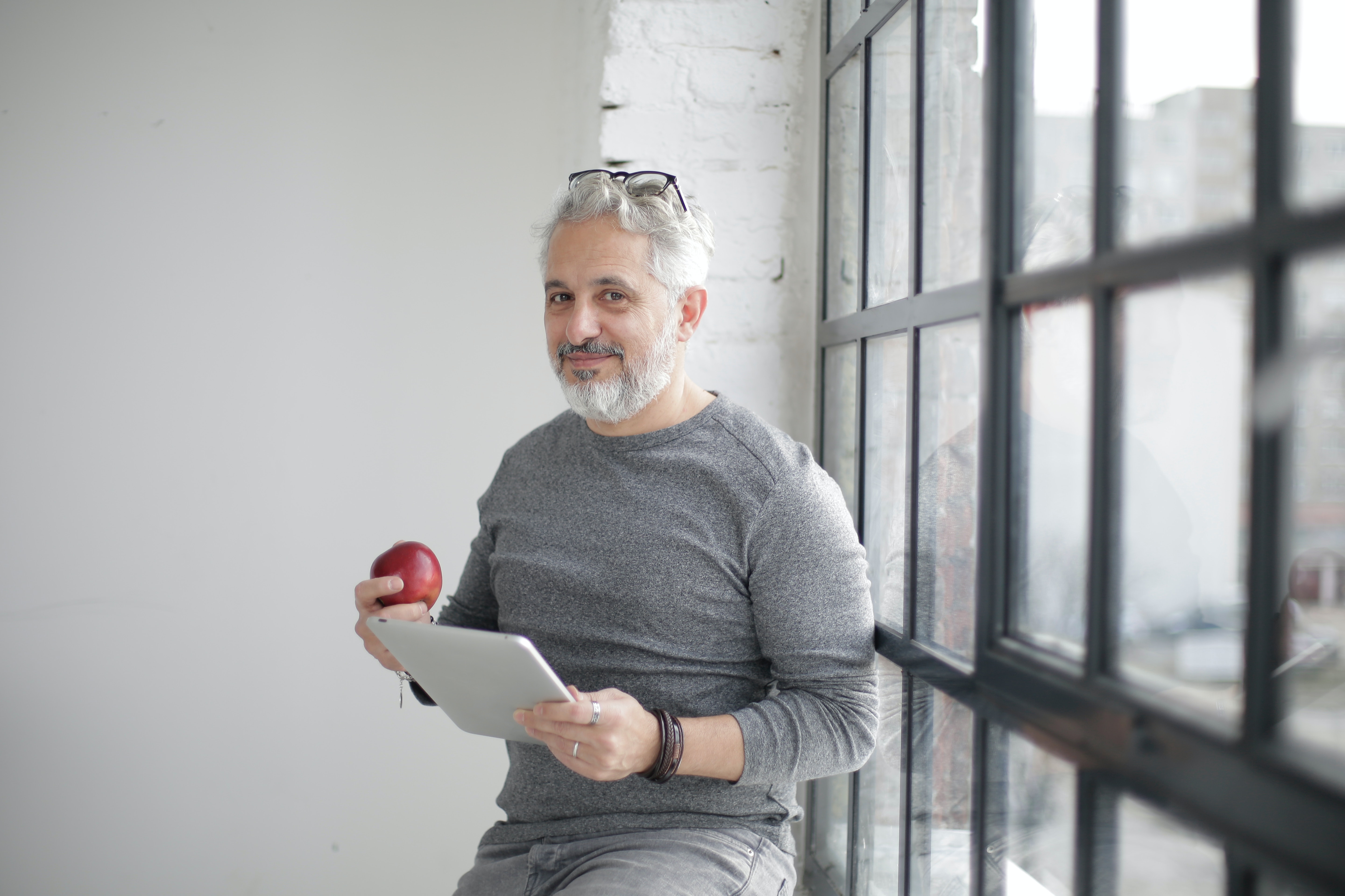 A smiling middle-aged man holds an apple and a tablet.