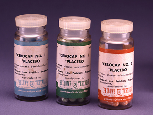 Uma fotografia mostra três frascos de vidro com comprimidos rotulados como placebos.