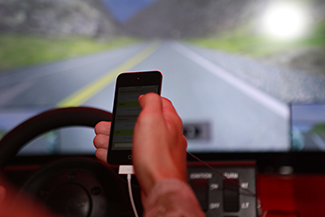 A mão direita de uma pessoa está segurando um telefone celular. A pessoa está no banco do motorista de um automóvel enquanto está na estrada.