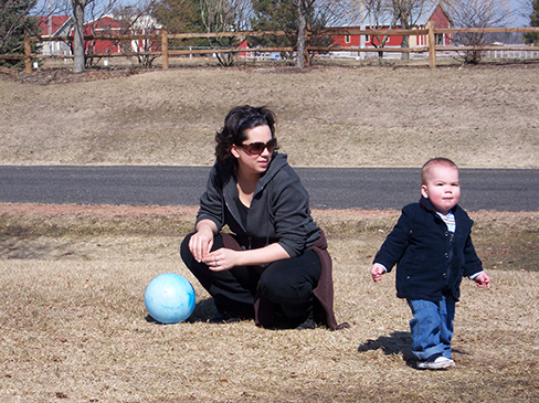 Uma fotografia mostra uma pessoa agachada ao lado de uma criança pequena que está em pé.