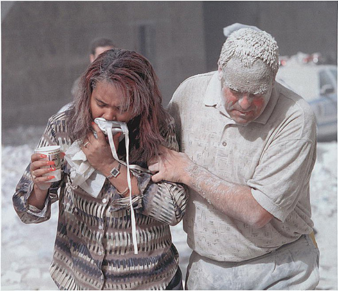 Uma fotografia mostra duas pessoas cobertas de poeira; uma parece estar ajudando a outra.