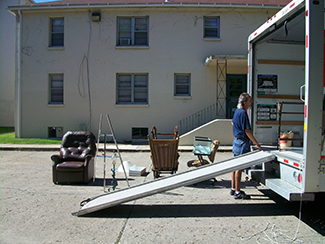 Una foto muestra a una persona junto a la parte trasera de un camión de mudanza descargando muebles.