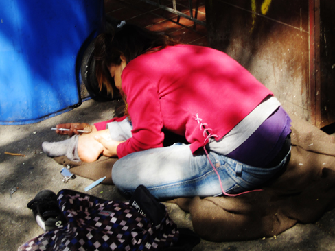 Une photographie montre une personne s'injectant de l'héroïne par voie intraveineuse avec une aiguille hypodermique insérée dans sa cheville.