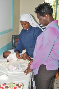 una foto de una madre y su bebé en un consultorio médico. El bebé recibe una inyección de inmunización de una enfermera