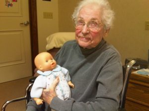 An elderly woman is holding a baby doll.