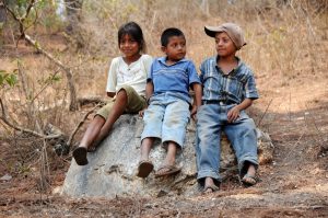 photo of three children sitting on a large rock outside