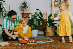Photo of a mother with her toddler son and daughter playing with trains