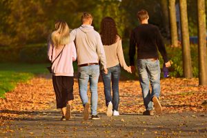 Two young adult couples walk together with one couple holding hands and the other with arms around each other