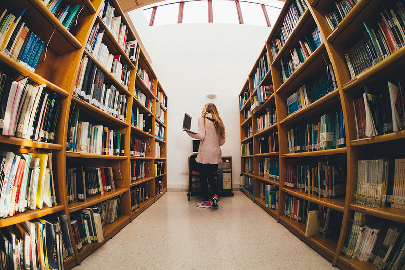 woman holding a laptop in between shelves of books at a library