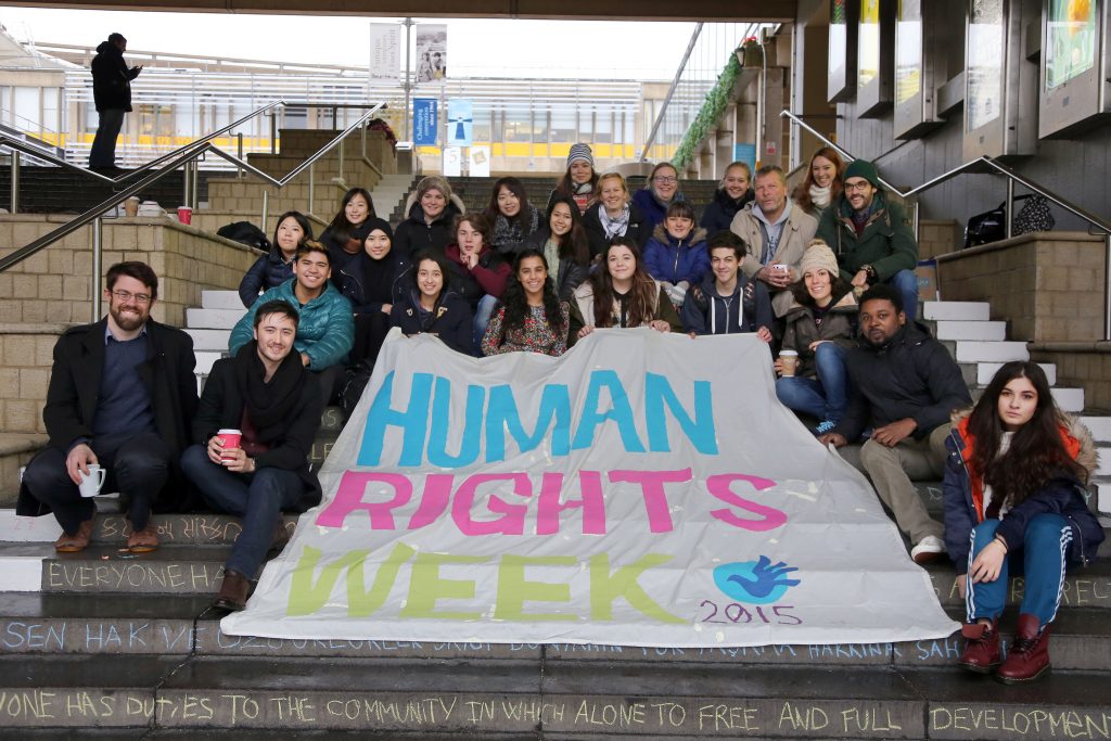 Photo of young people sitting on stairs holding a Human Rights Week banner