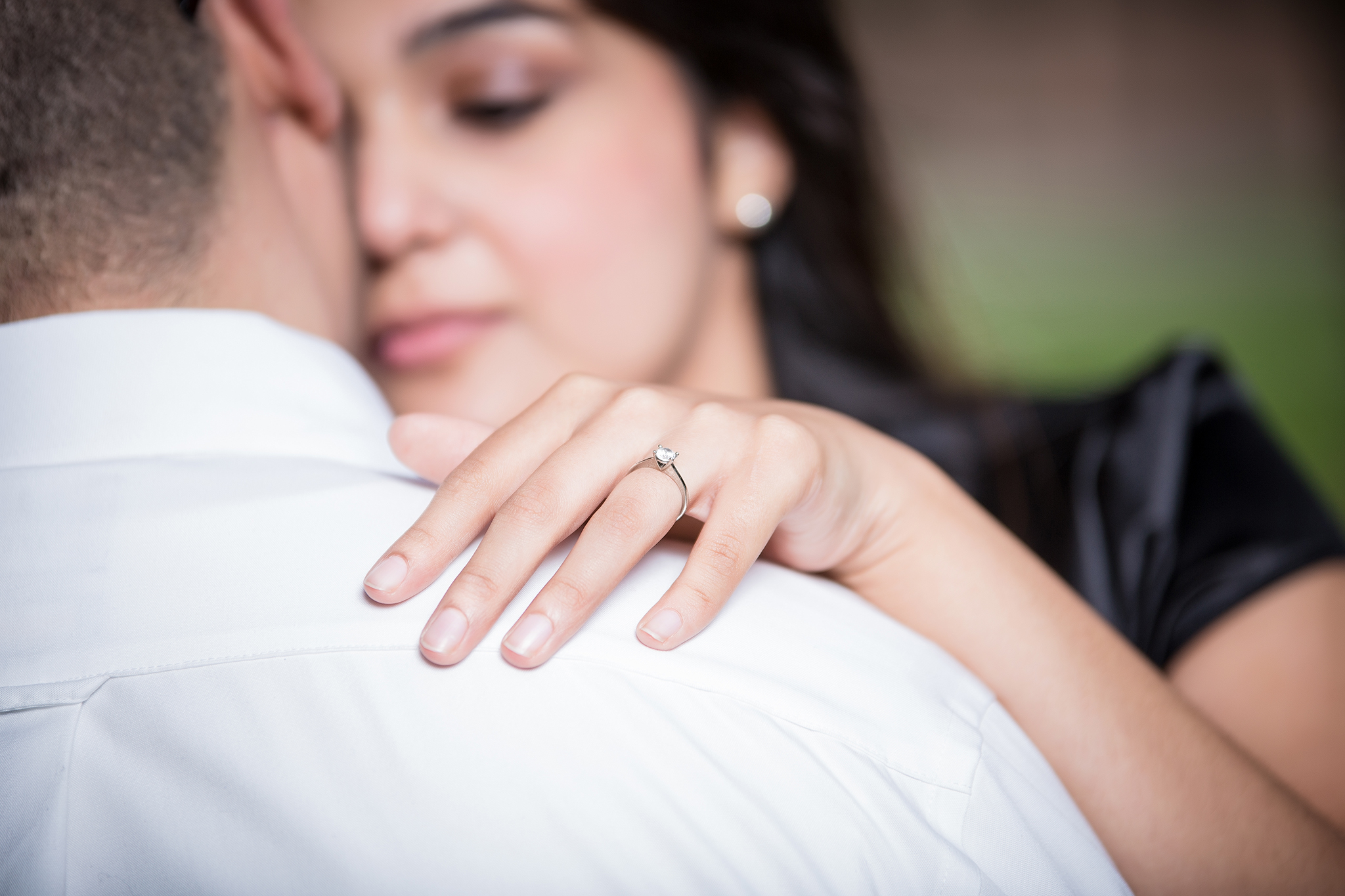 A man's shoulder with a woman looking at him with her hand on his shoulder and a ring on her finger.