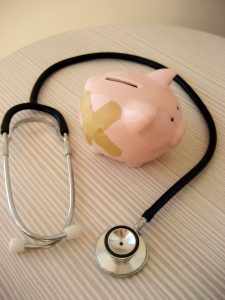 Art photo of a stethoscope and a piggy bank with two band-aides on it.