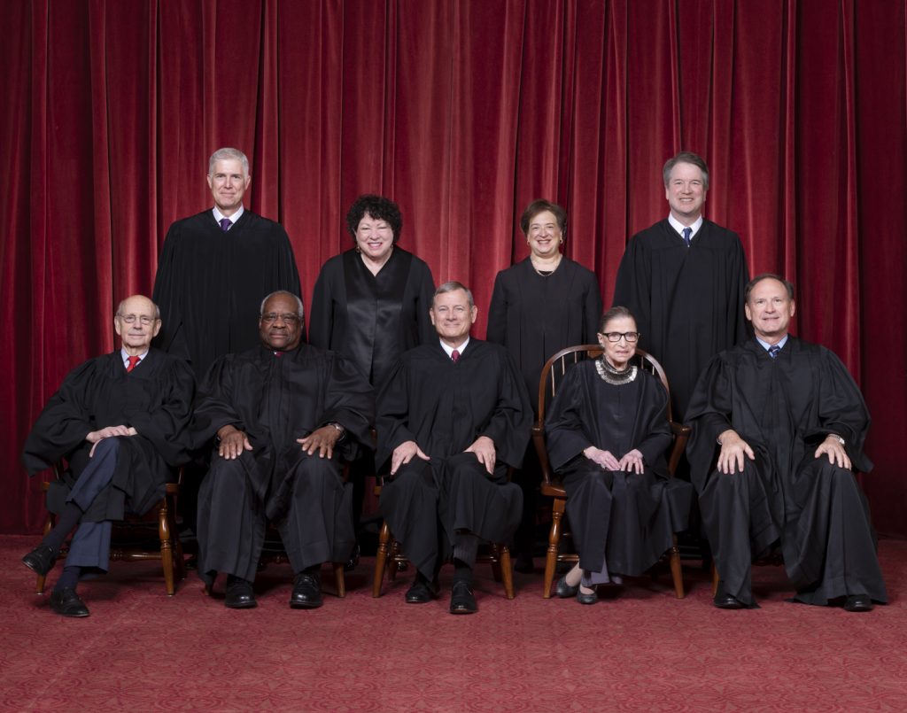 Nine Supreme Court Justices in black robes posing in front of a red curtain.