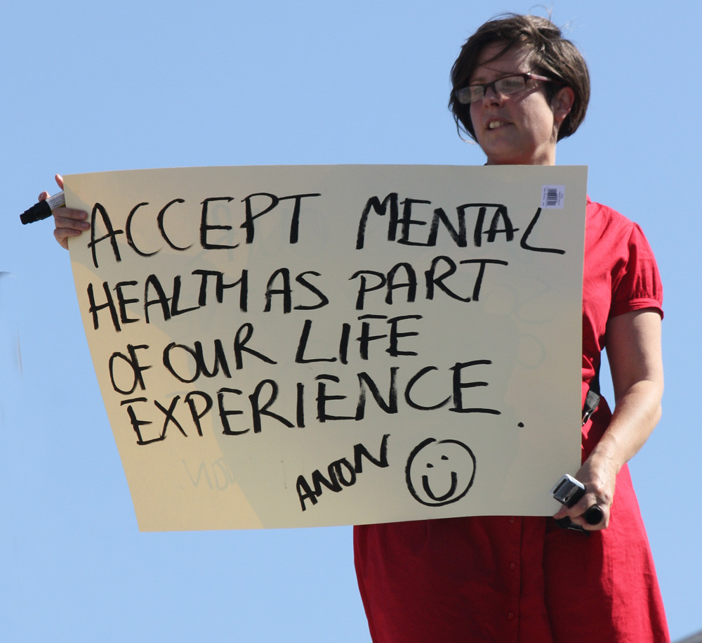 Woman in red dress holding sign that says Accept Mental health as part of our life experience.