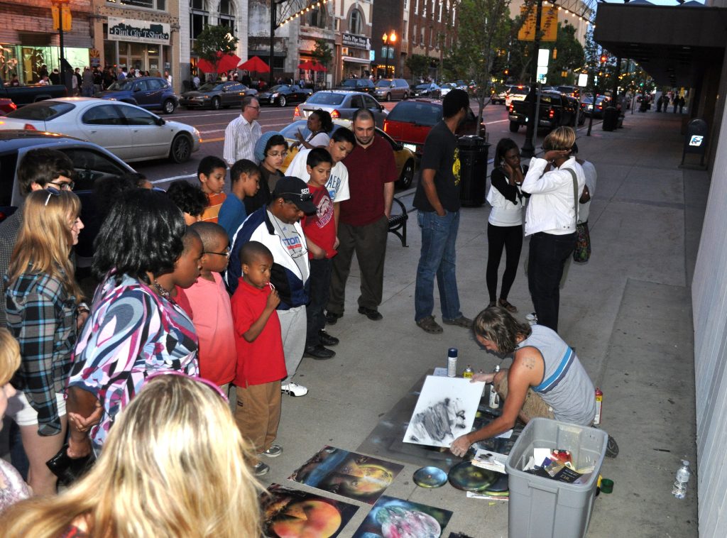 Photograph of people on the streets watching an artist making art.
