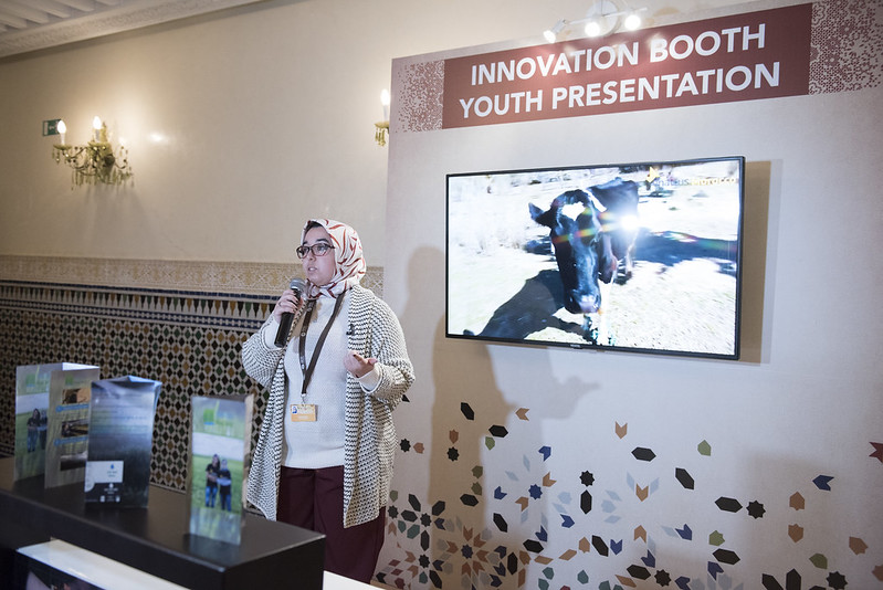 woman speaking an an Innovation Booth Youth Presentation with a picture of a cow on a screen behind her and broscures on the table in front of her