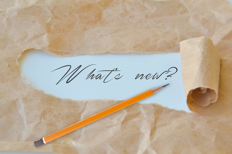 a pencil and a ripped paper bag revealing the words "What's new?" underneath.