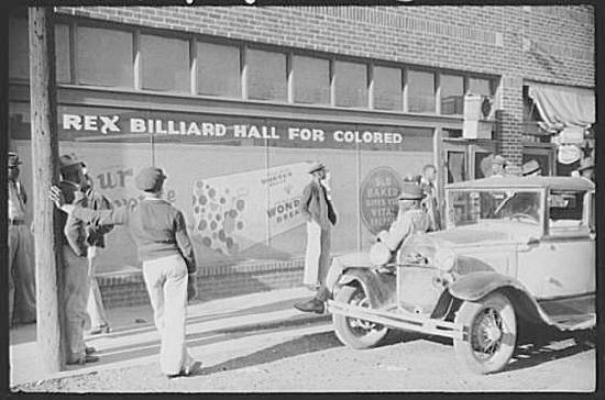 A group of Black men and an old car standing outside a billiard hall.