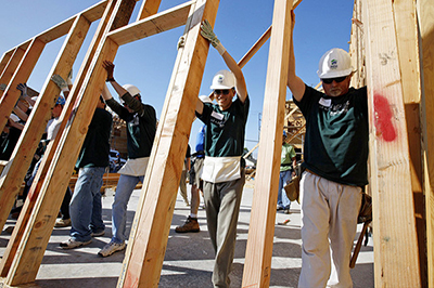 Volunteer construction workers raising the wall of a house together