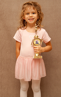Young girl in pink ballet clothing smiling abd posing with a gold trophy.