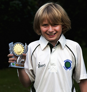 Boy smiling as he poses with a gold Cricket trophy.