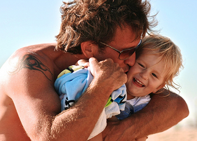 Father hugging and kissing the cheek of a broadly smiling son, a toddler.